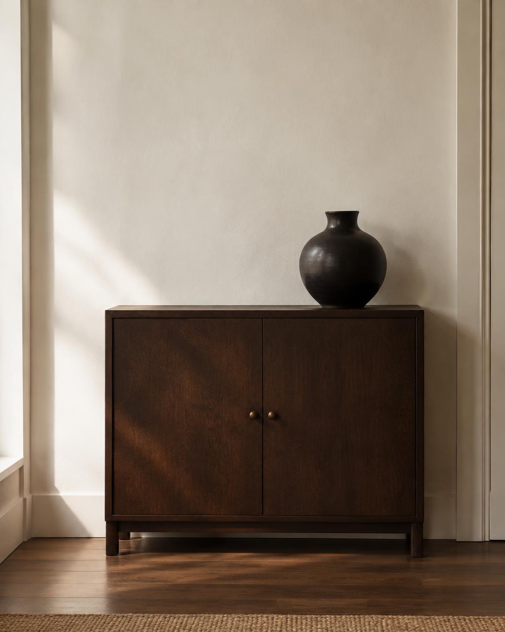 Dunkles Holzsideboard mit schwarzer Vase vor hellem Putz